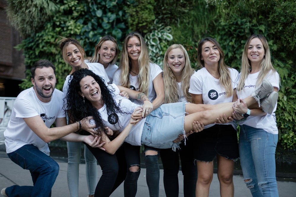 grupo de la empresa AUssieYouTOO en un evento en madrid. Todos llevan la camiseta de YouTOOProject de color blanca. Están sonriendo y sujetando a Marta Caparrós